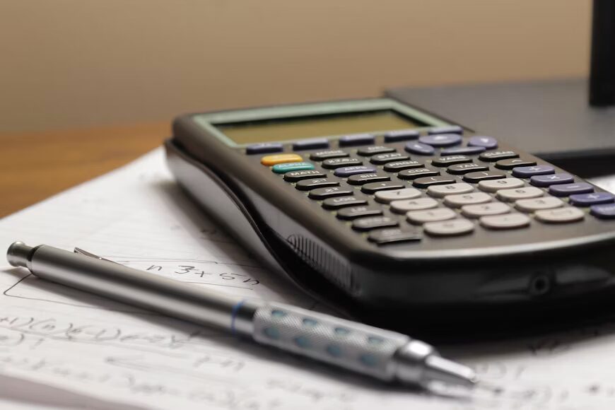 Calculator and invoice next to a laptop showing how to calculate the total landed cost of an overseas purchase.